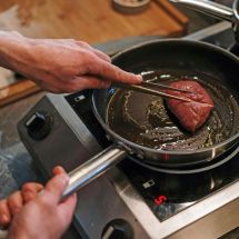 person cooking meat on portable induction cooktop