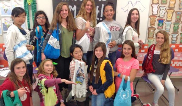 group of students in classroom holding up bags made from old t-shirts