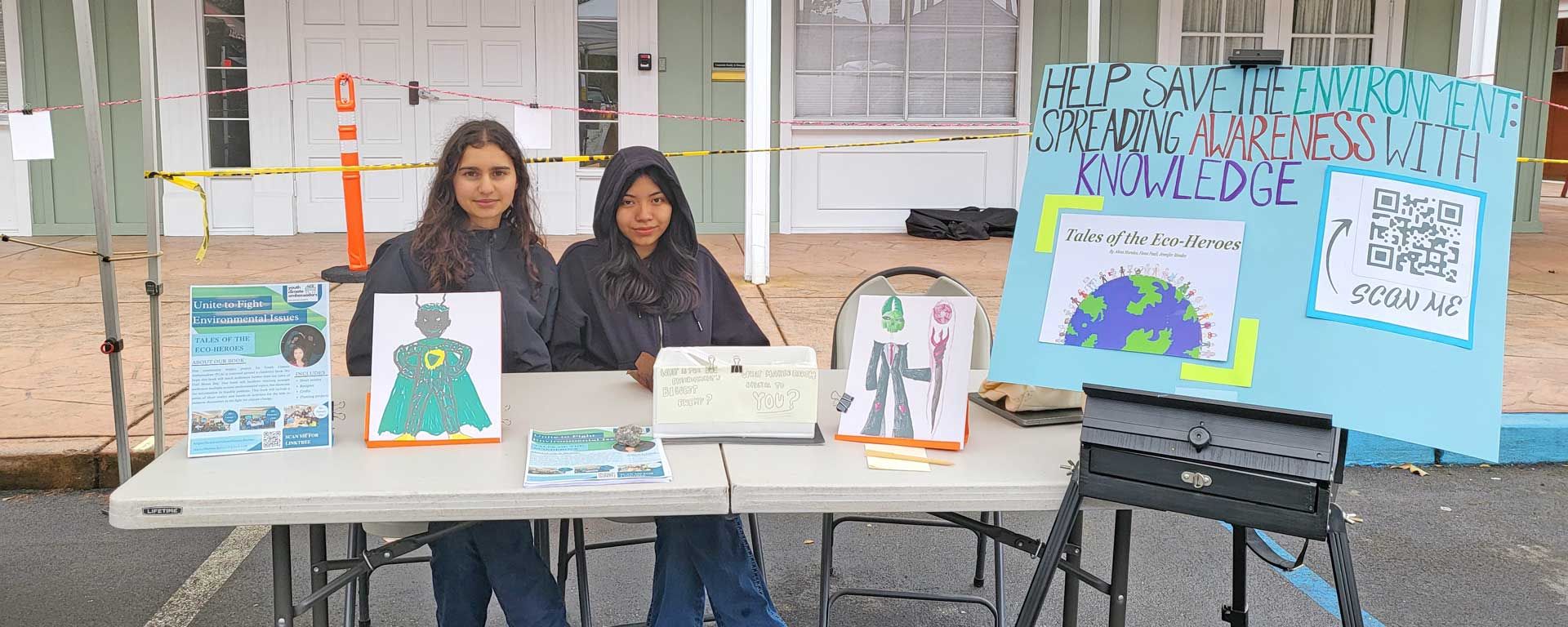 two students at event table displaying project titled Help Save the Environment - Spreading Awareness with Knowledge