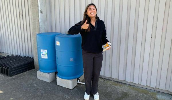 student posing in front of rain barrels giving thumbs up sign