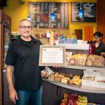 owner of 3 Bees Coffee in San Mateo County holding Green Business Certification inside his cafe